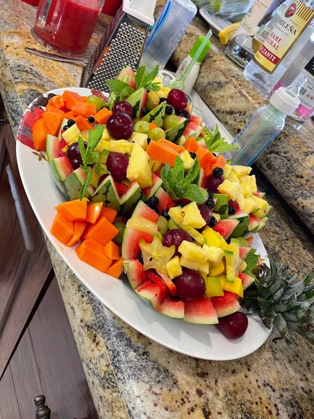 Platter of cut watermelon, pineapple, papaya, grapes and mint on a kitchen counter