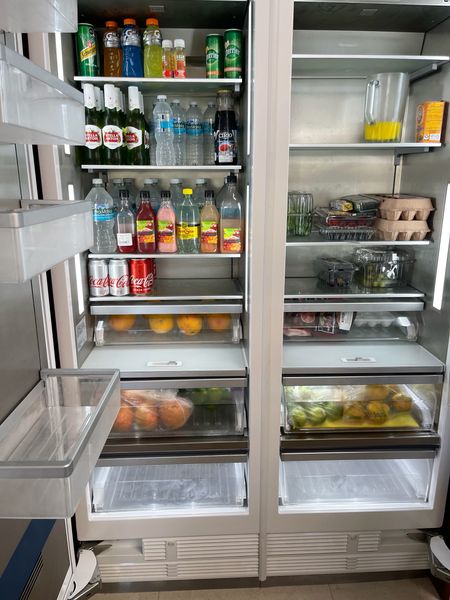 Double-door refrigerator stocked with bottled water, juices, sodas, eggs, oranges and fresh produce